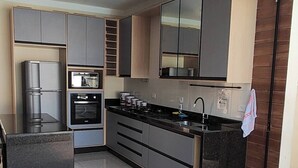 A modern kitchen with built-in appliances, a large island, and a sliding glass door leading to a balcony. - House with HEATED POOL (No additional cost) (Bopiranga Itanhaém)