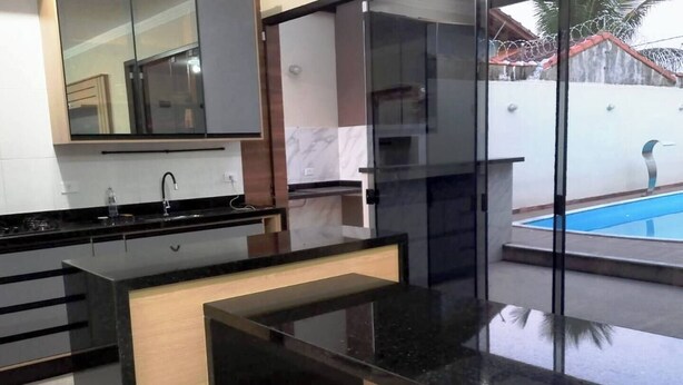 A modern kitchen with a black countertop, wooden drawer, and a glass backsplash. - House with HEATED POOL (No additional cost) (Bopiranga Itanhaém)