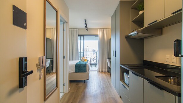 A hotel room with a bed, a desk, a kitchenette, and a view of the city through the window. - Modern Studio Near Allianz Parque Sp-p1610a (São Paulo)