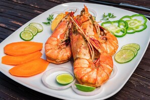 Une assiette de homards cuits, accompagnés de tranches de carotte et de citron vert, et décorée de rondelles de concombre et de persil.
