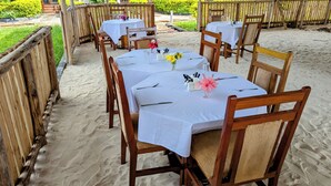 A beachside restaurant with multiple tables set for dining, each covered with white tablecloths and wooden chairs. - Crown View Hotel (Nungwi)