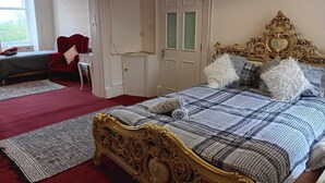 A bedroom with a large bed, a red chair, a wardrobe, and a door.