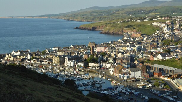 A coastal town with a marina, historic buildings, and a hilly backdrop.