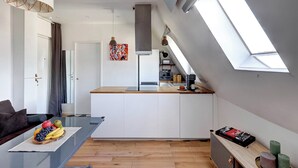 A modern kitchen with a central island, a dining area with a glass table, and a living space with a sofa. - Champs-Élysées - 1BR (Paris)