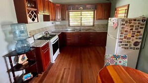 A kitchen with wooden cabinets, a water dispenser, a stove, and a refrigerator with magnets. - Castaway Blue Hole Long Caye, Belize (Long Caye Lighthouse Atoll  Belize City)