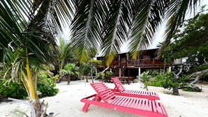 A beach area with a red lounge chair and a wooden structure in the background. - Castaway Blue Hole Long Caye, Belize (Long Caye Lighthouse Atoll  Belize City)