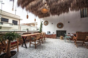 An outdoor patio with a rustic thatched roof, a dining table with chairs, and a seating area with cushions. - Vega 43 Hostel (Sarande)