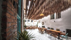 An outdoor patio with brick walls, wooden furniture, and a thatched ceiling. - Vega 43 Hostel (Sarande)