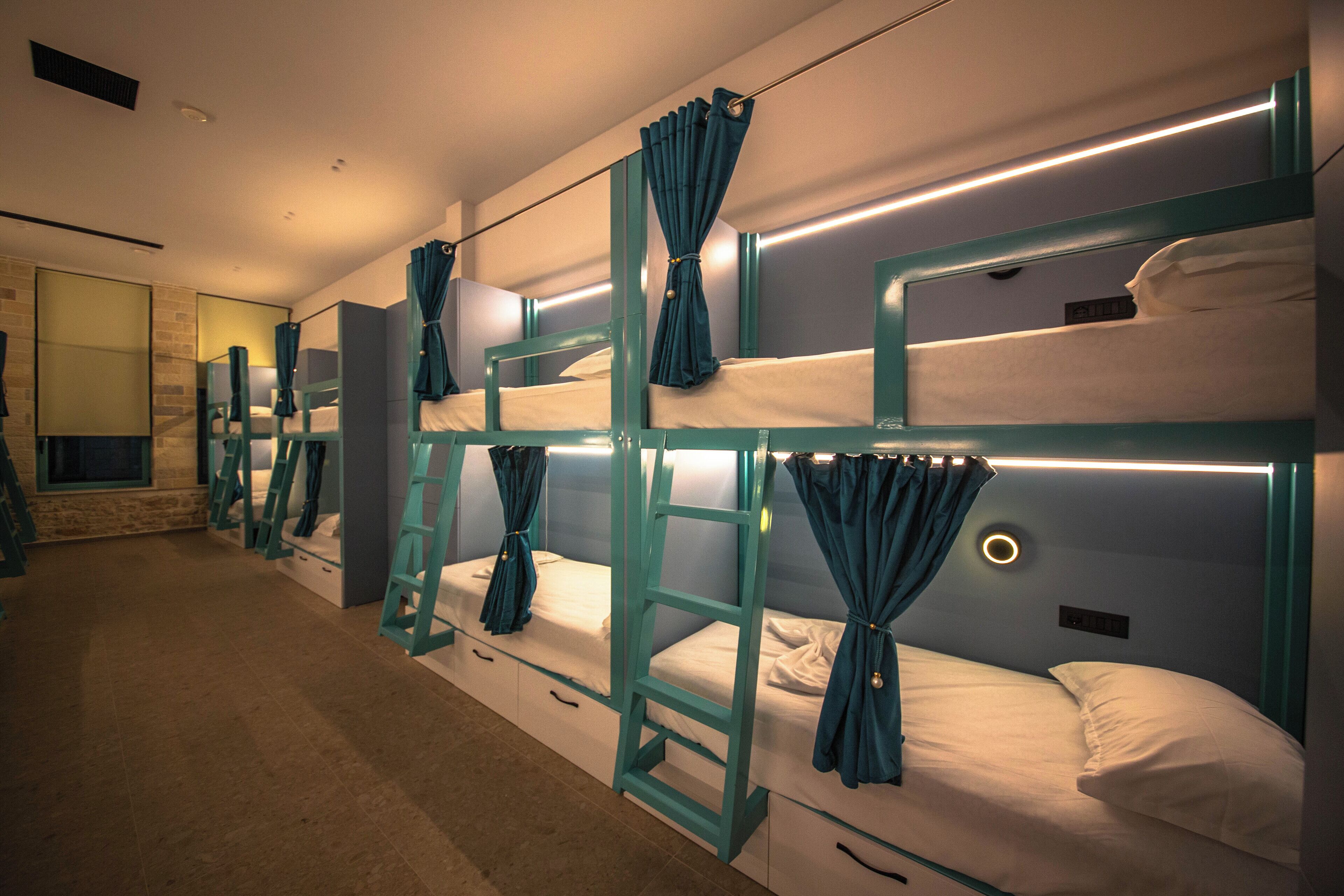 A row of bunk beds with curtains, a ladder, and a mirror on the wall.