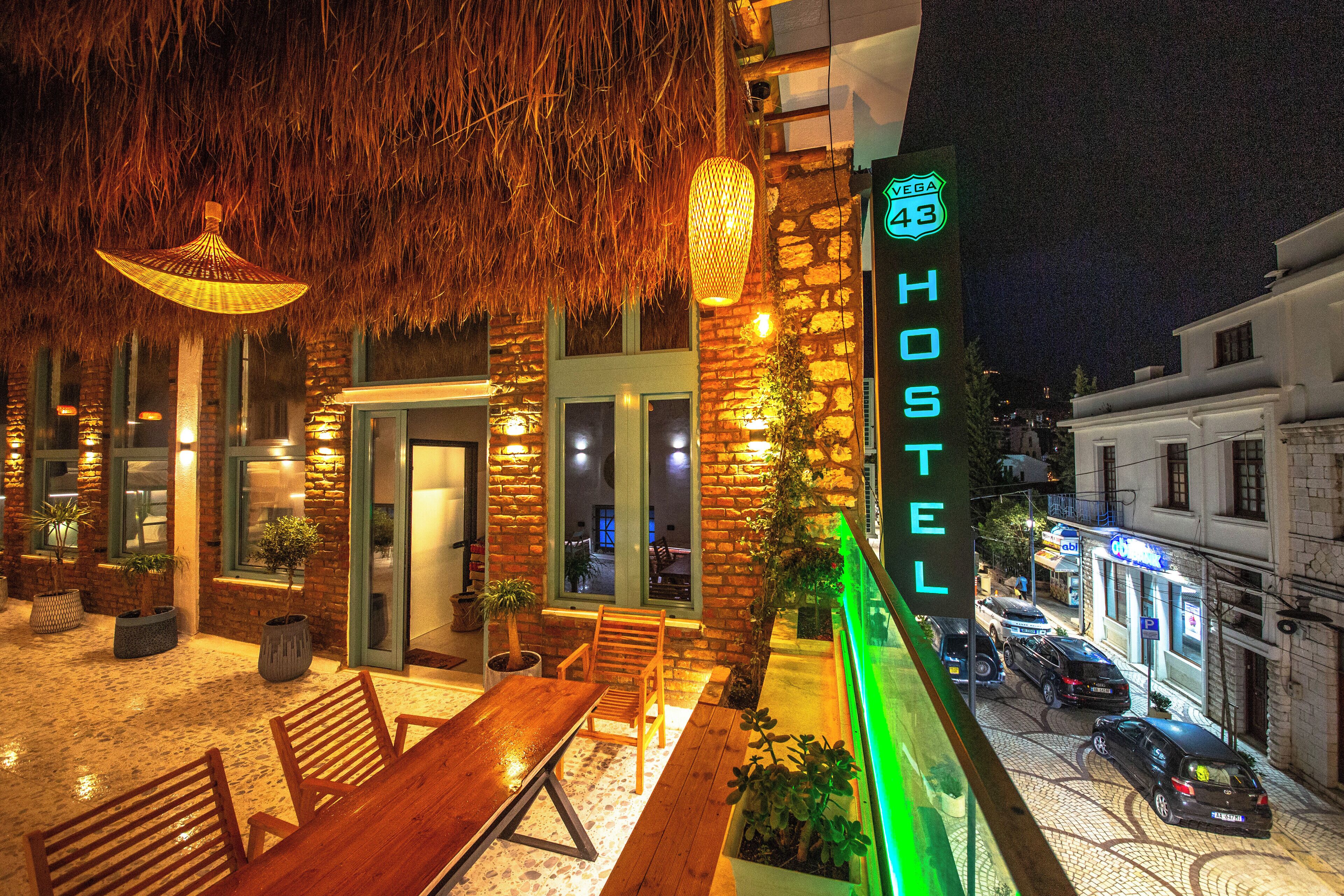A hostel with a stone facade, outdoor seating, and a neon sign.