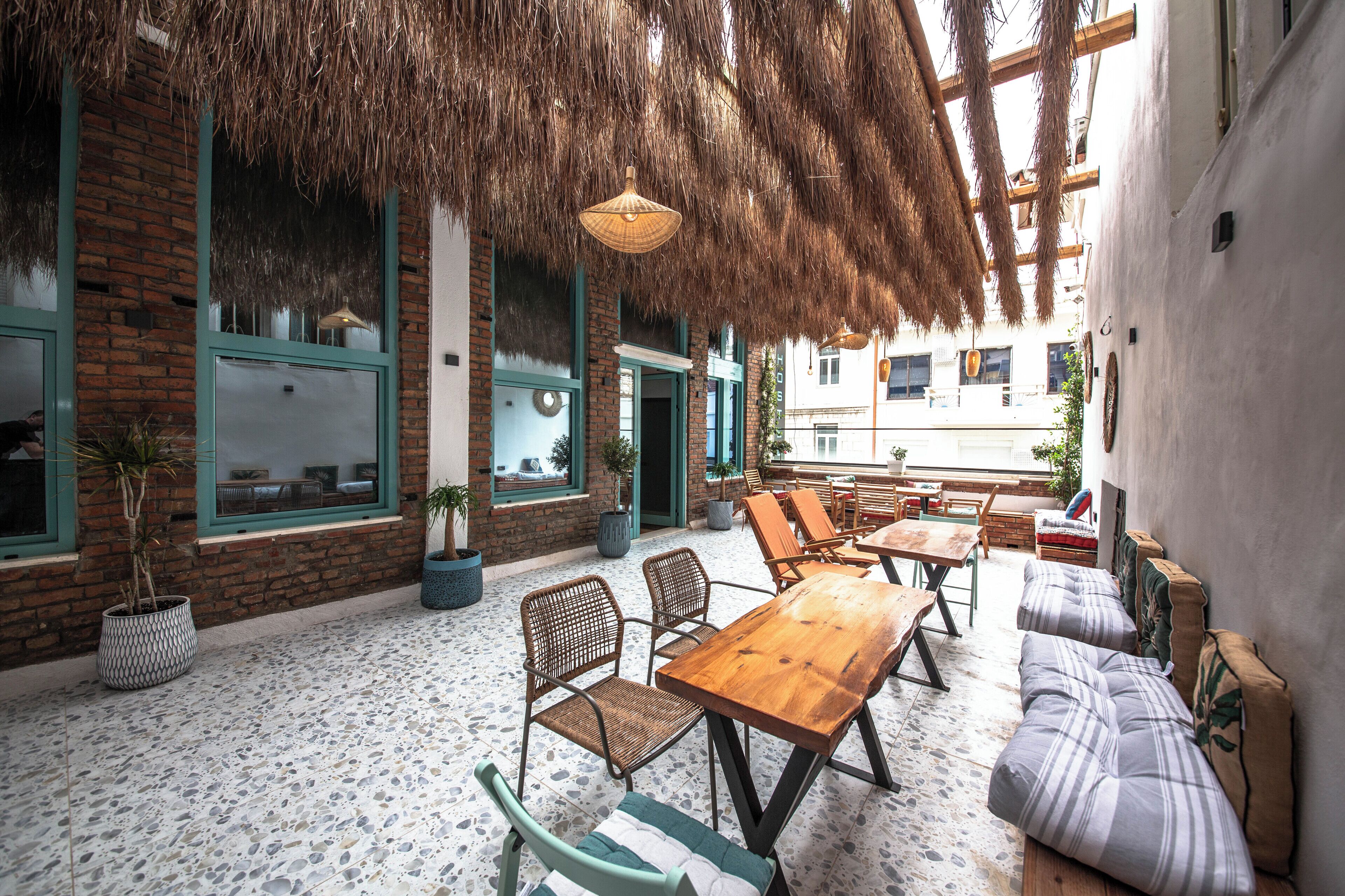 An outdoor seating area with a wooden table and chairs, potted plants, and a thatched roof.