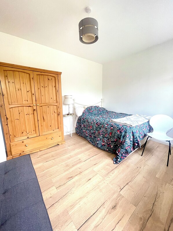 A room with a bed, a wooden wardrobe, a white chair, and a hanging light fixture.