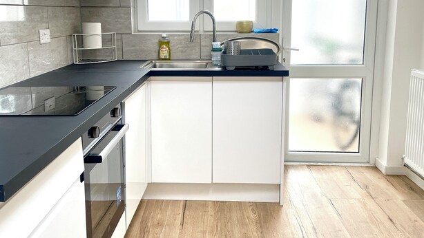 Una cocina moderna con gabinetes blancos, encimera negra, horno empotrado, pileta y candelabro.