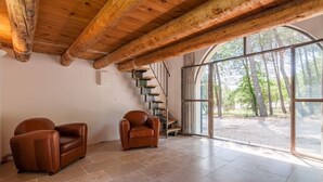 A spacious room with a wooden ceiling and a large window offering a view of trees. There are two leather chairs and a staircase leading to an upper level. - Magnificent stone farmhouse (murs)