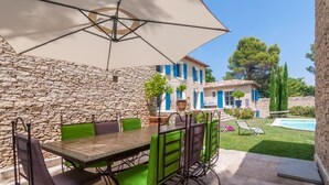 An outdoor patio with a stone wall, a table with chairs, and a pool in the background. - Magnificent stone farmhouse (murs)