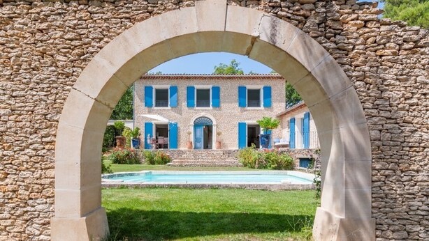 A stone archway framing a building with a pool and a well-maintained lawn. - Magnificent stone farmhouse (murs)