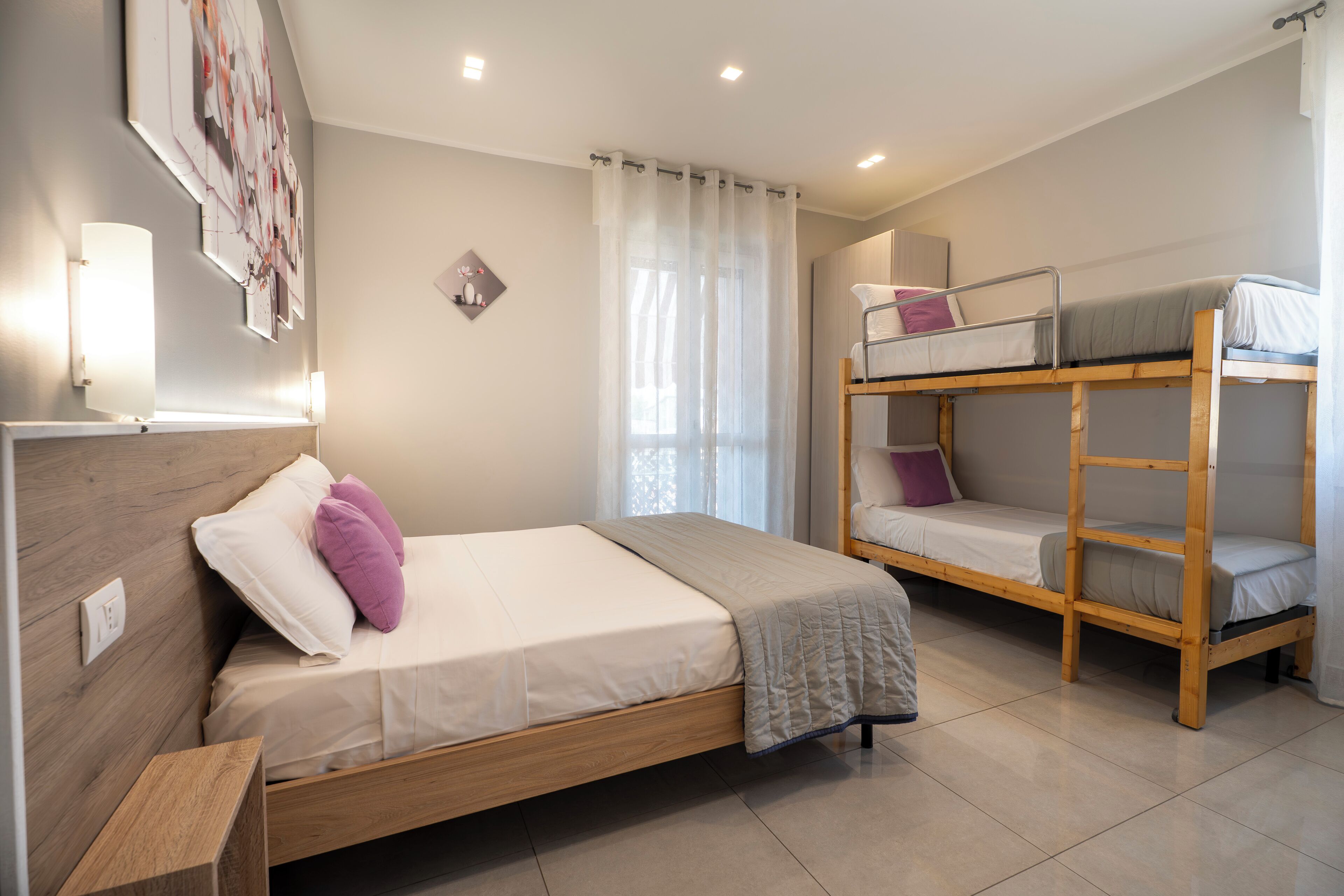 Una camera da letto moderna con un letto singolo, un letto a castello, un comodino e un punto luce a parete.