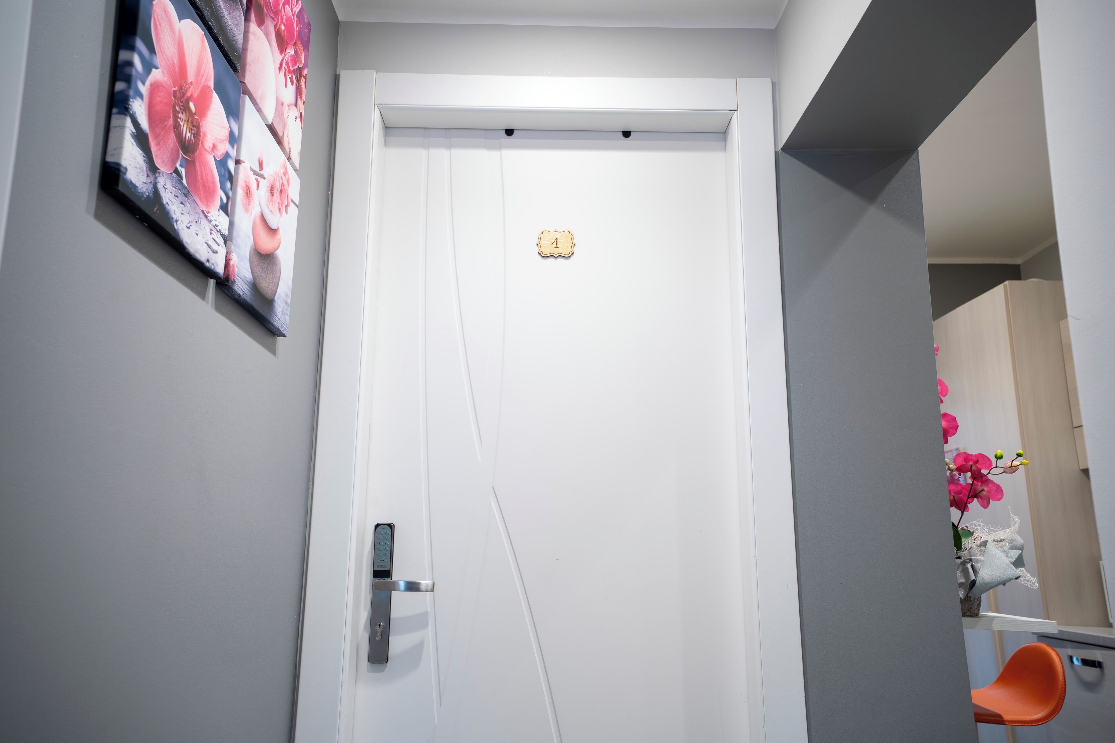A white door with a small plaque, a modern door handle, and a painting of flowers on the wall.