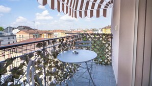 A balcony with a white table and chairs, surrounded by a metal railing and covered by a striped awning. - Affittacamere Orchidea (Modena)
