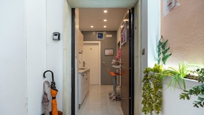 A narrow hallway with a metal bucket containing two umbrellas, a small table with a chair, and a potted plant on the right. - Affittacamere Orchidea (Modena)