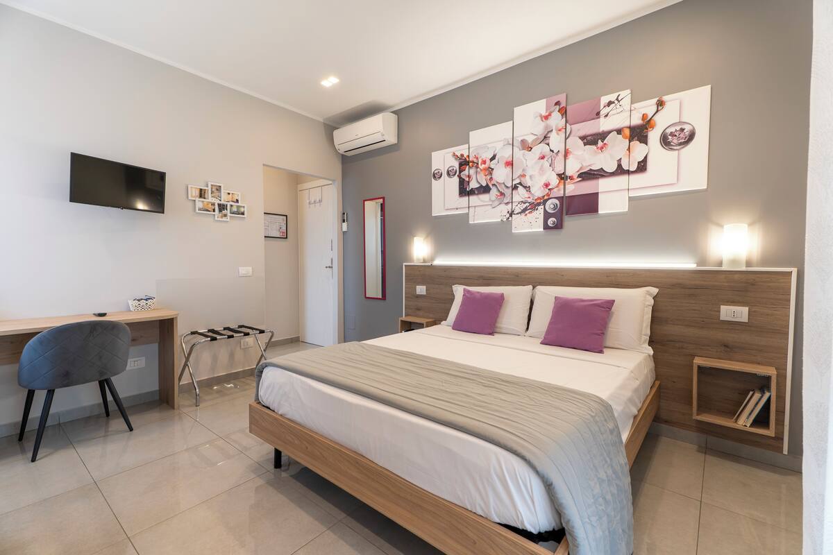 A modern bedroom with a bed, a desk, a chair, and a TV.