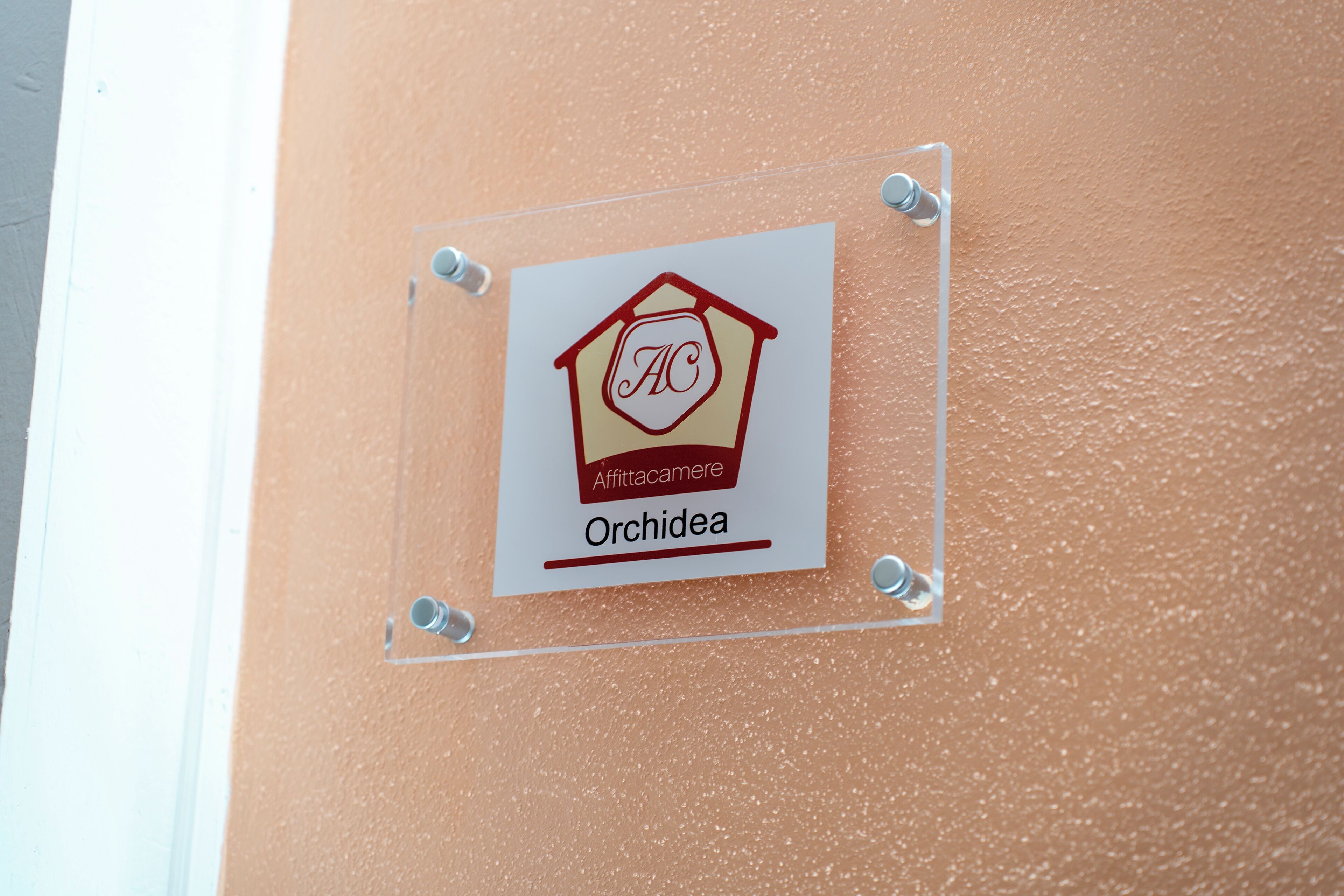 A sign with a logo and the name "Orchidea" on a textured wall.