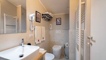 Ein Badezimmer mit Waschbecken, Toilette und Dusche. Handtücher und ein Fön sind an der Wand angebracht.