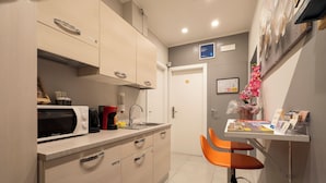 A compact kitchen with a microwave, toaster, and sink. There are two orange chairs and a small table with a vase of flowers. - Affittacamere Orchidea (Modena)