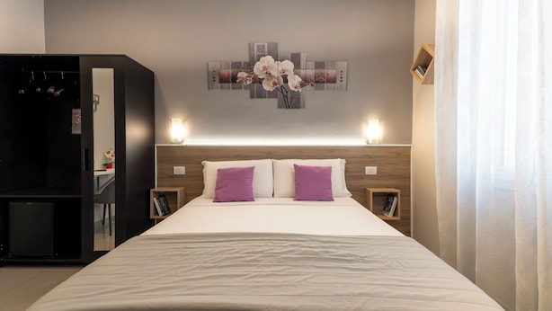 A neatly arranged hotel room with a bed, two bedside tables, a wall-mounted artwork, and a wardrobe. - Affittacamere Orchidea (Modena)