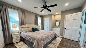 Un dormitorio con cama, ventilador de techo, cómoda, espejo y puerta.