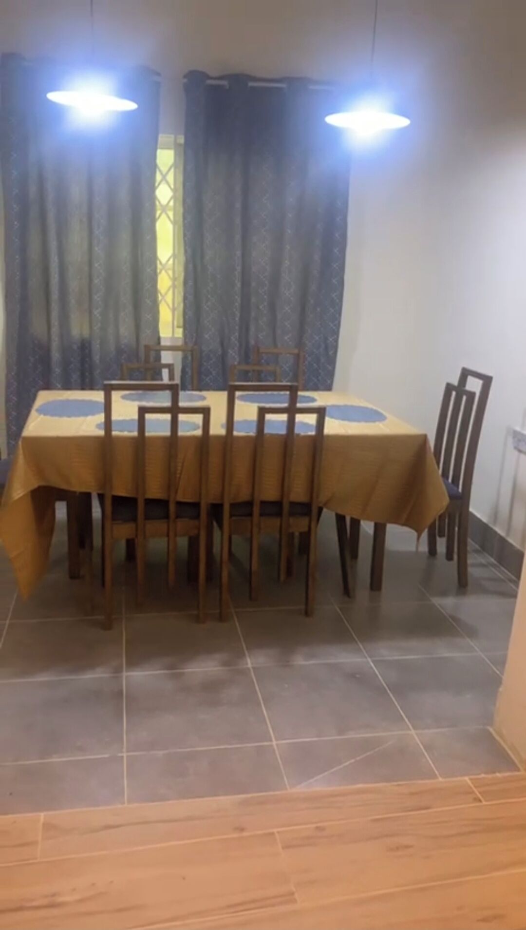 Un coin repas avec une table et des chaises, une fenêtre avec des rideaux et un sol carrelé.
