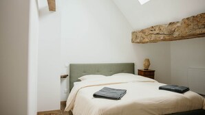 Ein Schlafzimmer mit einem Bett, einem Nachttisch, einer Lampe und einem rustikalen Steinbalken über dem Bett.