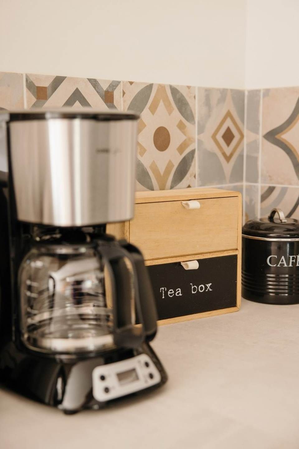 A coffee maker, a tea box, and a container labeled "CAFE" on a kitchen counter.
