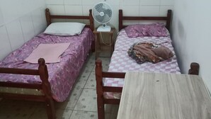 A small, tiled room with two wooden beds, a small table, and a standing fan.