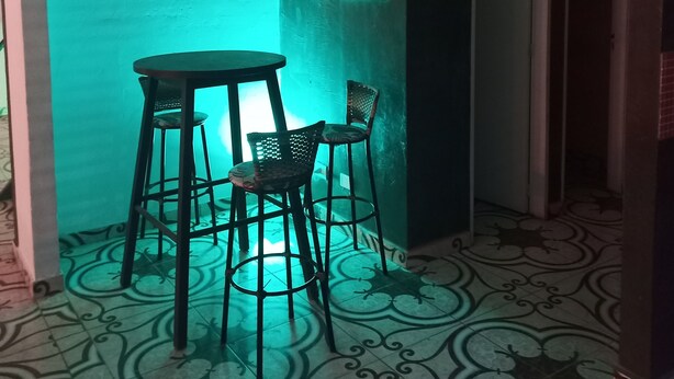 A room with a table and two chairs, a wall with framed pictures, and a patterned floor.