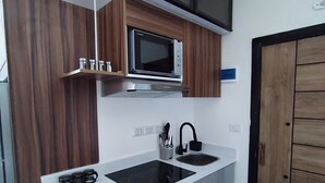 A compact kitchen with a microwave, stove, sink, and wooden cabinets. - A charming & ideal sea view studio apartment in  ,Hurgahda with a private beach (Red Sea Governorate)