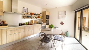 Een moderne keuken met houten kastjes, een centraal kookeiland met zitplaatsen en een uitzicht door een glazen deur op een buitenruimte.