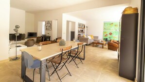 Een ruime woonkamer met een grote eettafel, comfortabele zithoek en een keuken in de achtergrond.