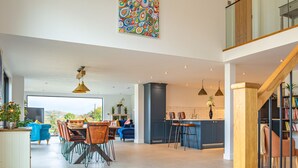 A spacious living area with a dining table, blue sofas, and a kitchen area with bar stools. - Beautiful Barn Conversion - Orchard Escape for 12 (Cropthorne)