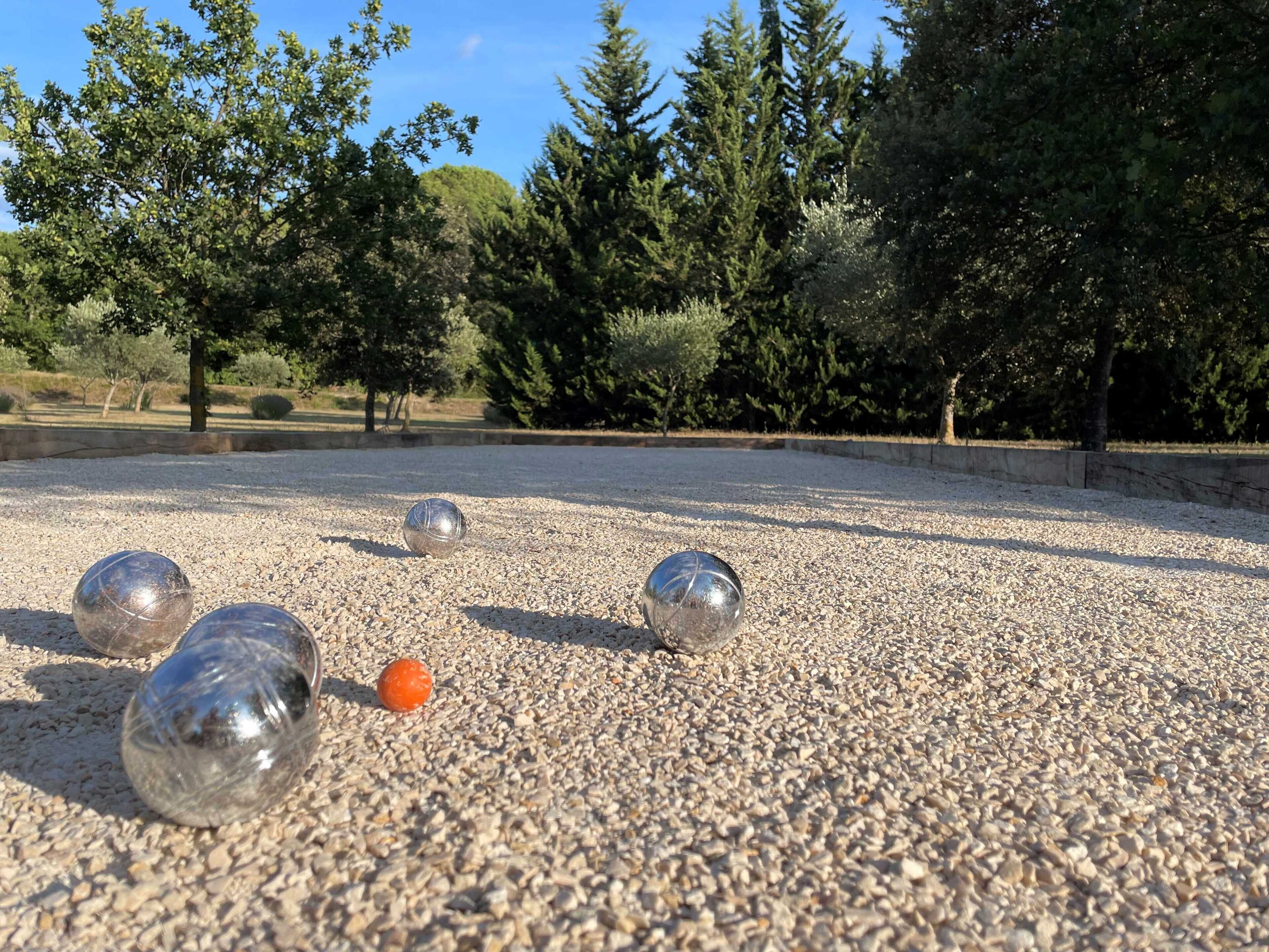 Un patio con suelo de grava, tres bolas metálicas y una naranja.