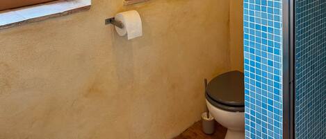 A bathroom with a wooden floor, a window, a tiled shower enclosure, and a shelf with toiletries.