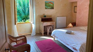 A bedroom with a bed, a desk, a chair, a radiator, and a window with curtains. - Gîte Mûrier (Suze-la-Rousse)