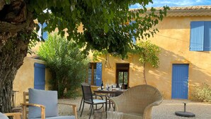 An outdoor seating area with wicker furniture, a table set for dining, and a blue door in the background. - Gîte Mûrier (Suze-la-Rousse)