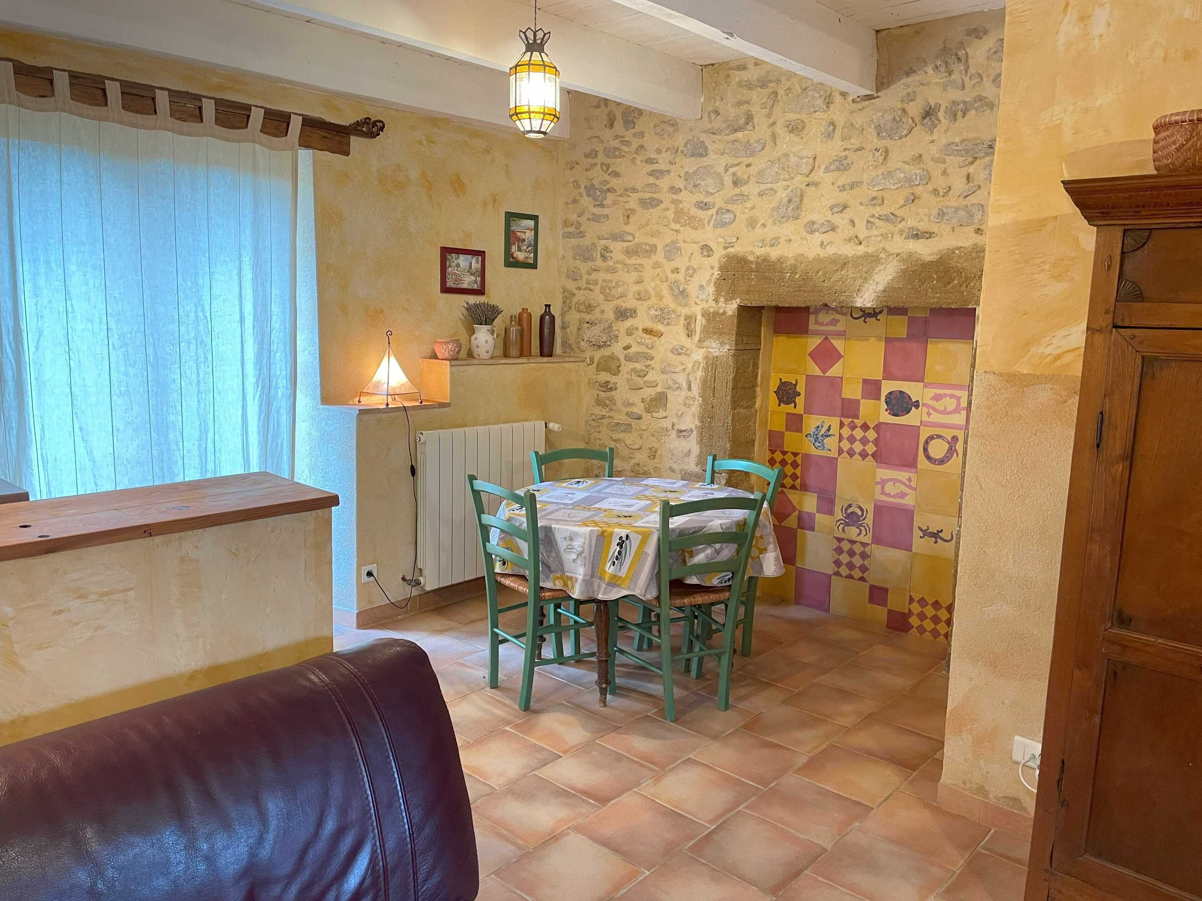 Ein gemütlicher Essbereich mit einem Tisch für zwei Personen, umgeben von grünen Stühlen. Eine Holztheke ist links sichtbar, und eine Steinwand mit einem gefliesten Kamin ist rechts.