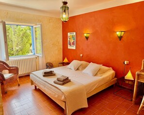 Un dormitorio con cama, ventana, silla y lámpara de pared.