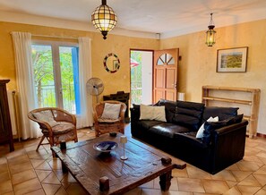 Un salon comprenant un canapé, deux fauteuils, une table, un ventilateur et une porte donnant sur l’extérieur.