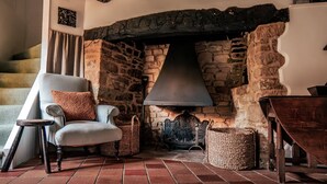 Ein gemütliches Wohnzimmer mit Kamin aus Stein, einem bequemen Sessel und einem Holztisch.