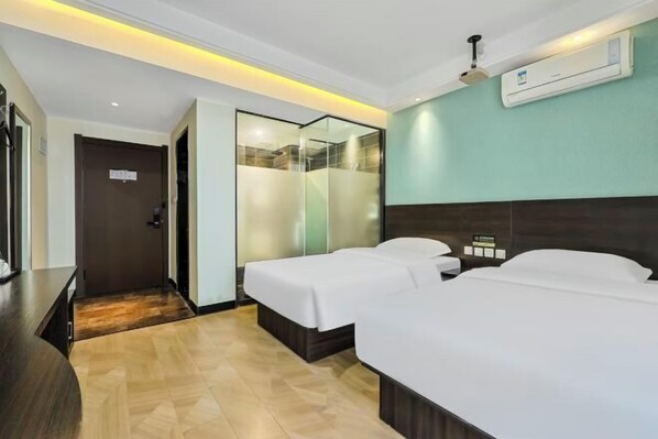 A hotel room with two single beds, a wooden desk, a mirror, and an air conditioning unit on the wall.