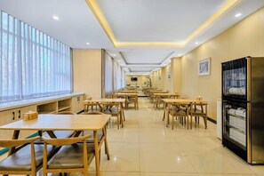 Un comedor con varias mesas y bancos, un refrigerador y un ventanal con persianas.