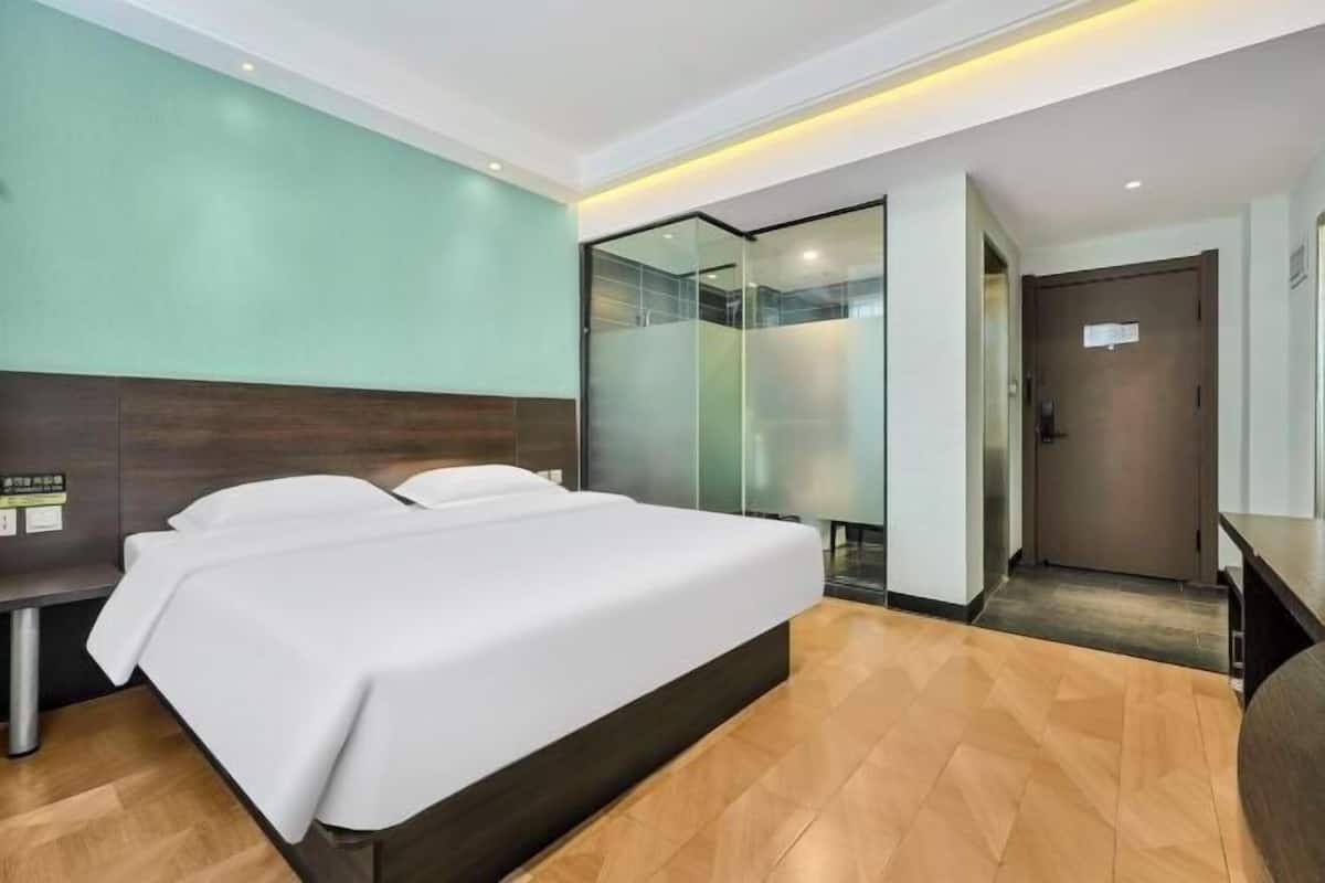 A hotel room with a large bed, a desk, and a glass partition.
